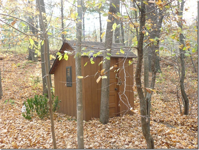 Exterior of light brown outhouse with asymmetrical roof
