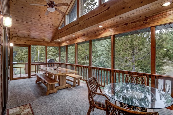 Screen porch with wood railing and wood dining table with benches