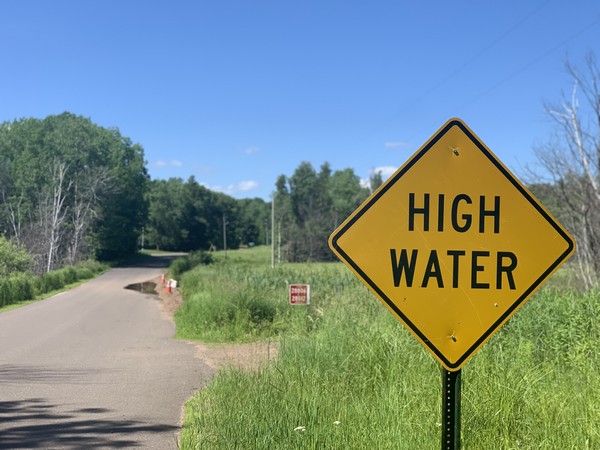 High water sign near road with water covering part of it
